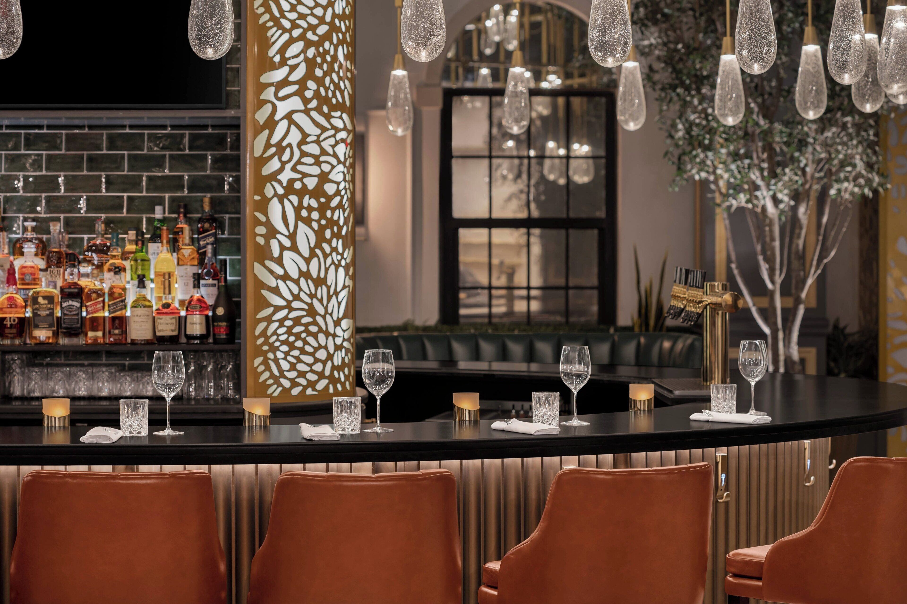A bar area with a black countertop, brown leather chairs, and a variety of bottles on shelves.