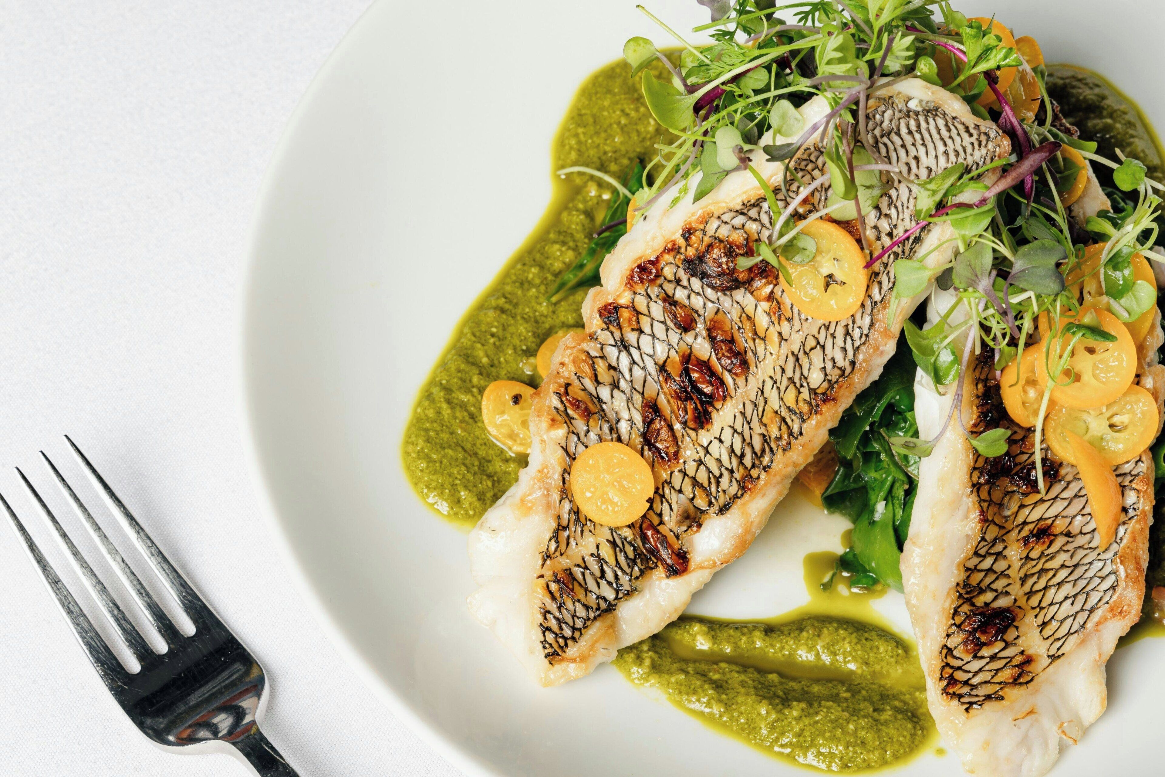 A plate of grilled fish with greens and a fork.