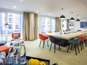 Una habitación de hotel moderna con un ventanal grande, un área de comedor con sillas coloridas y una mesa con botellas de agua y vasos.