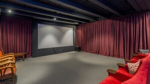 A home theater room with a large screen, red curtains, and wooden chairs. - Finns (Paekakariki)