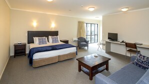 A hotel room with a large bed, a desk with a TV, a sofa, and a small table. - Finns (Paekakariki)