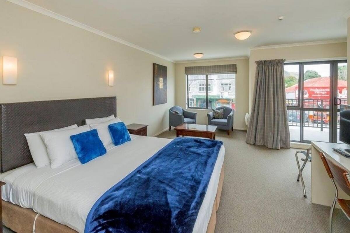 A hotel room with a large bed, a desk, a chair, a TV, and a window with curtains.