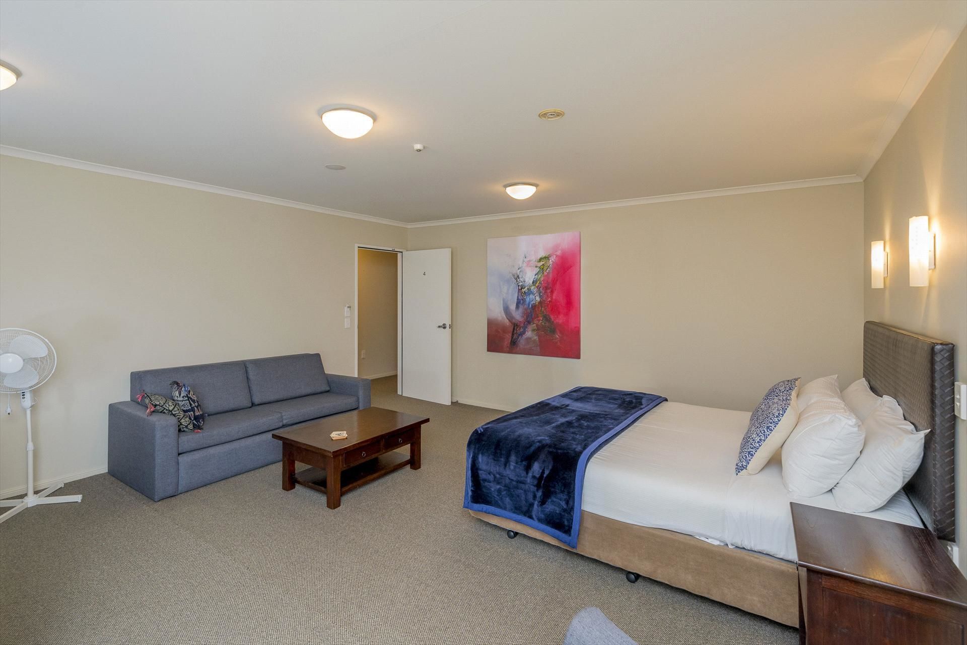 Una habitación de hotel con cama, sofá, una mesita y un ventilador de pie.