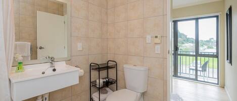 A bathroom with a white sink, a toilet, and a mirror. There is a window with a view of a balcony.