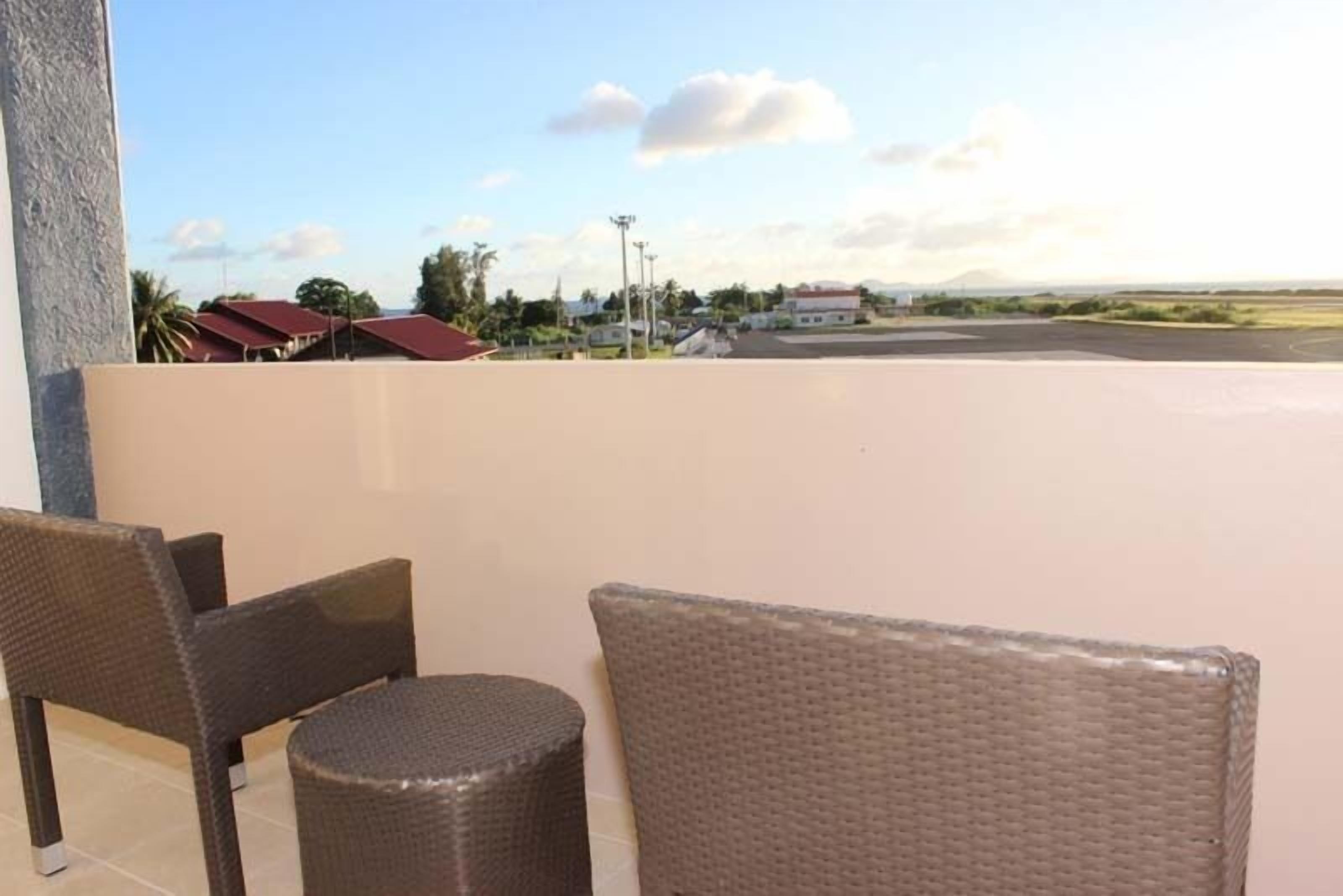 A balcony with wicker furniture and a view of a parking area and buildings in the distance.