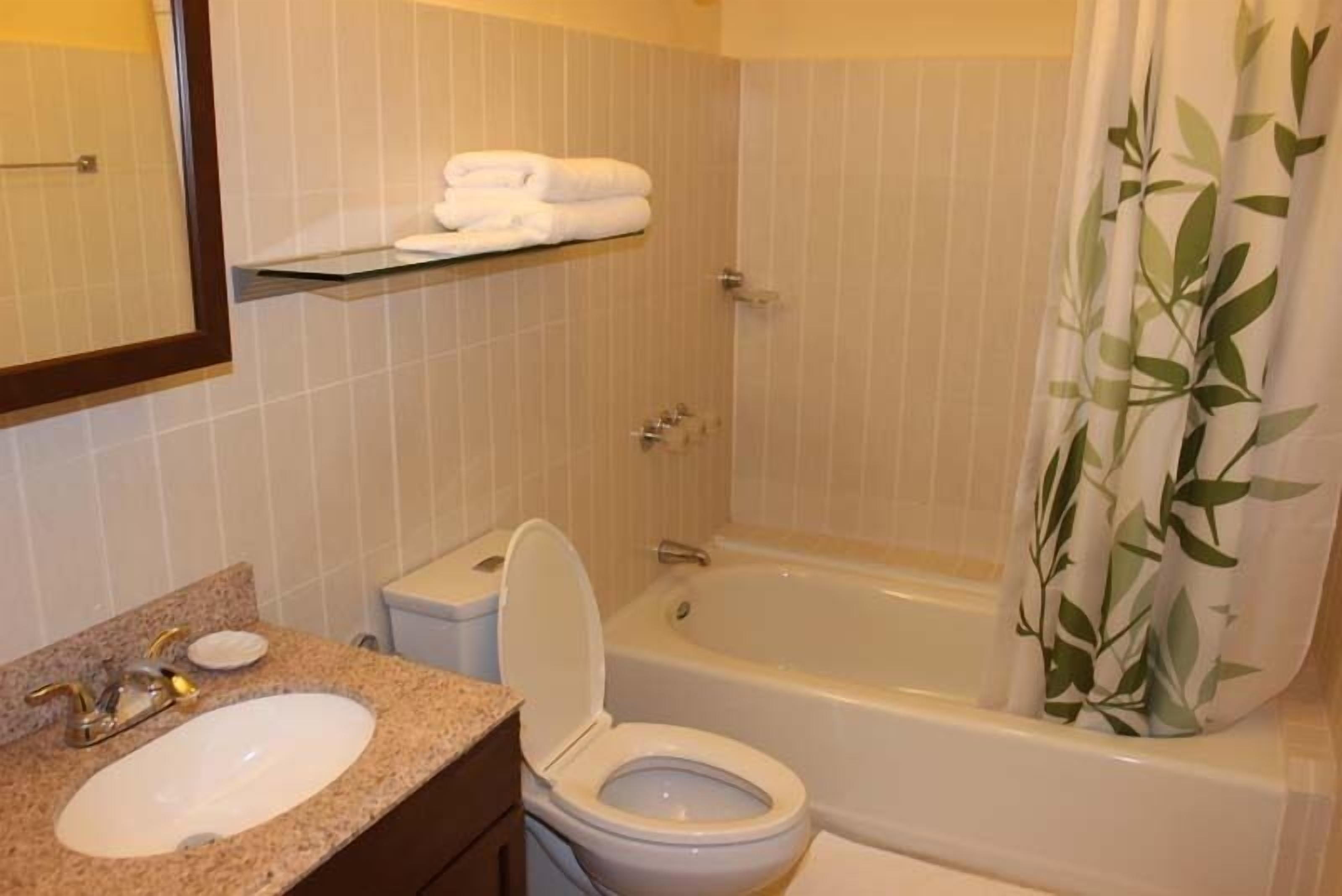 Een badkamer met een wastafel, toilet en bad. Boven het toilet bevindt zich een plank met handdoeken.