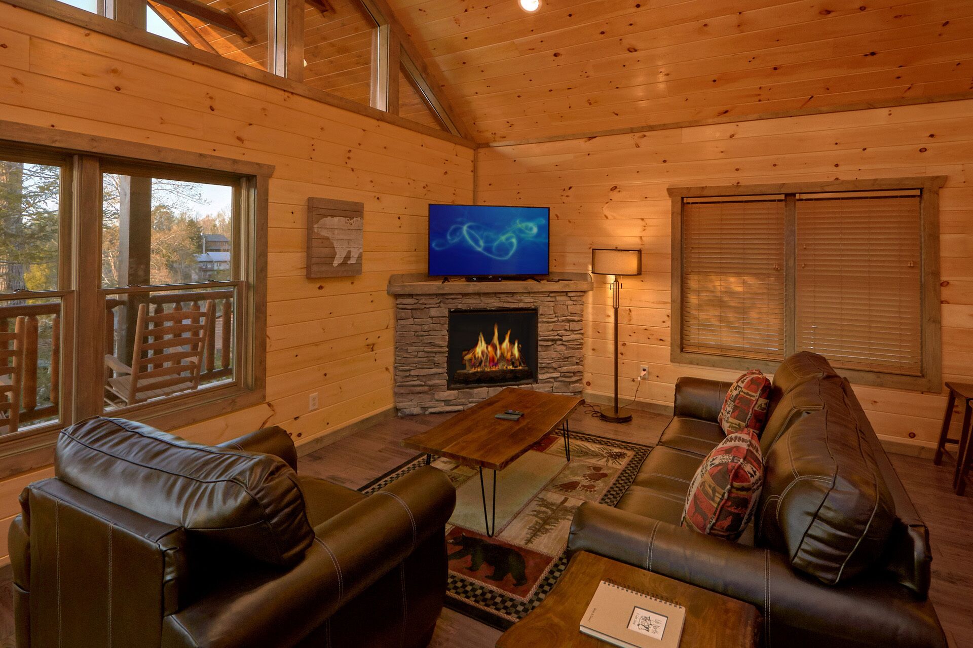 A cozy cabin interior with a stone fireplace, leather furniture, and a television mounted above it.