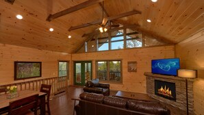 A log cabin interior with a fireplace, leather sofa, dining table, and a television.