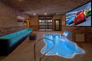 Un espace spa comprenant une piscine, un canapé bleu et un téléviseur diffusant des dessins animés mettant en scène des voitures.