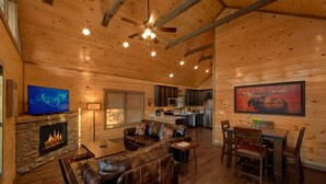 A cozy cabin interior with a stone fireplace, leather sofa, dining table, and a kitchen area.