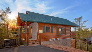 A log cabin with a stone foundation, wooden exterior, and a green roof.