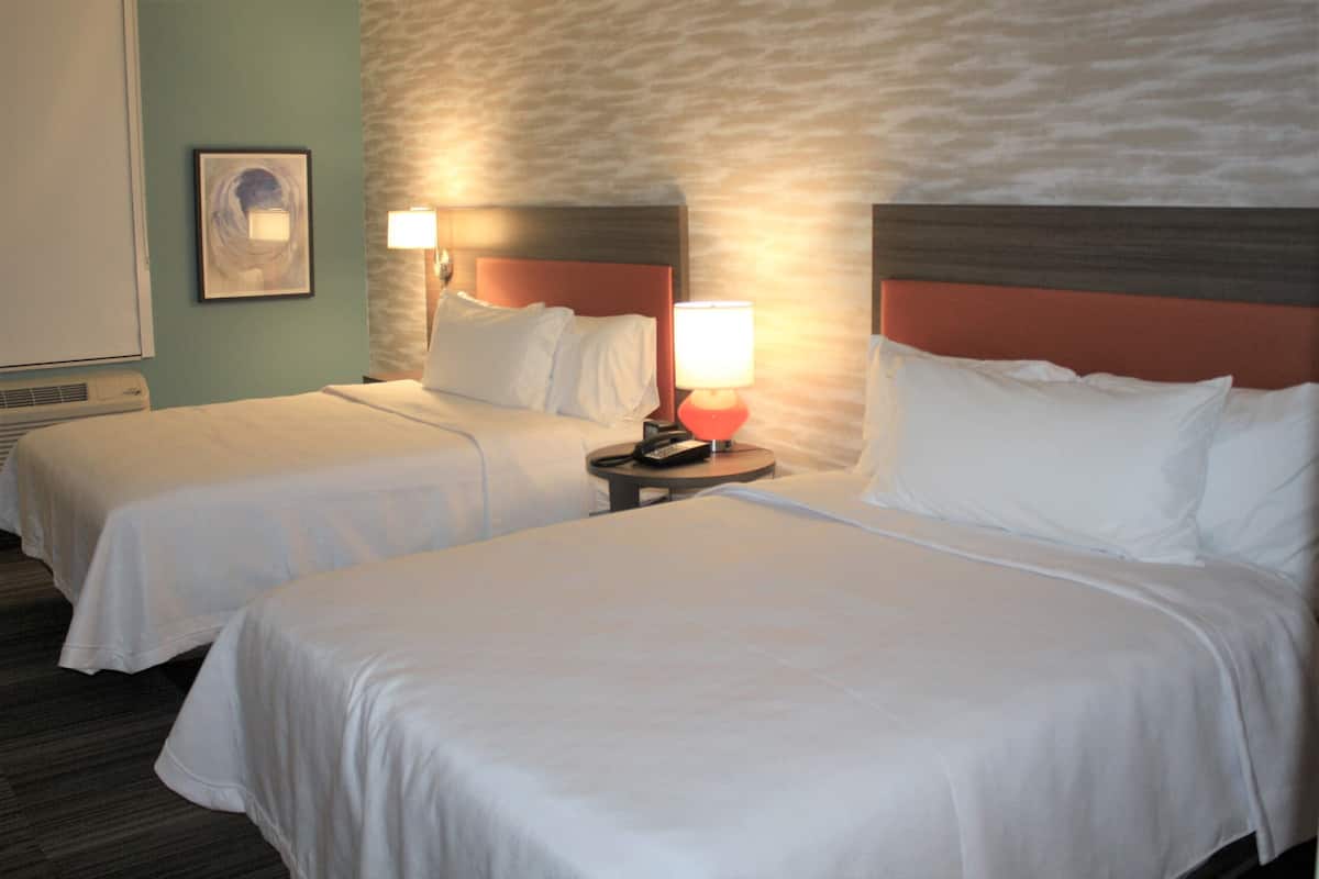 Een hotelkamer met twee bedden, een nachtkastje met een lamp en een kunstwerk aan de muur.