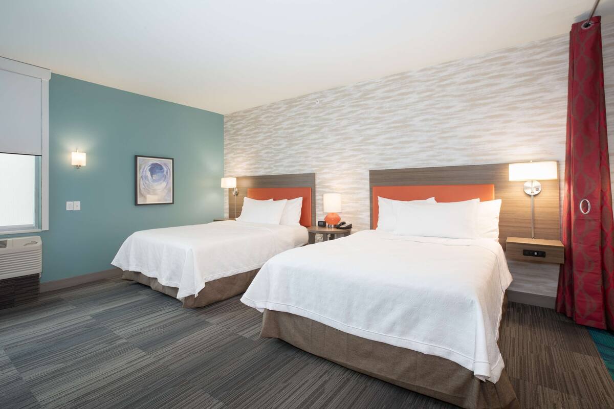Een hotelkamer met twee bedden, een groot raam en een rood gordijn.