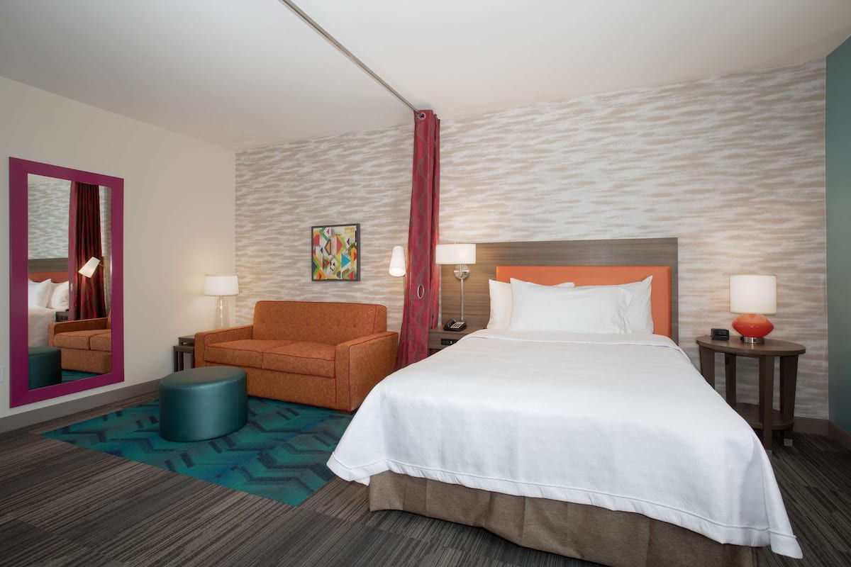 Een hotelkamer met een groot bed, een slaapbank, een stoel, een klein poufje, een spiegel en een lamp.