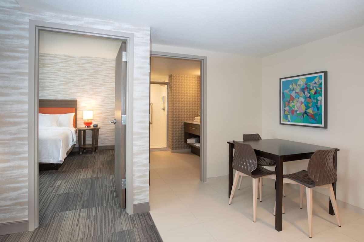 Een hotelkamer met een bed, nachtkastje, lamp en een zithoek met een tafel en stoelen.