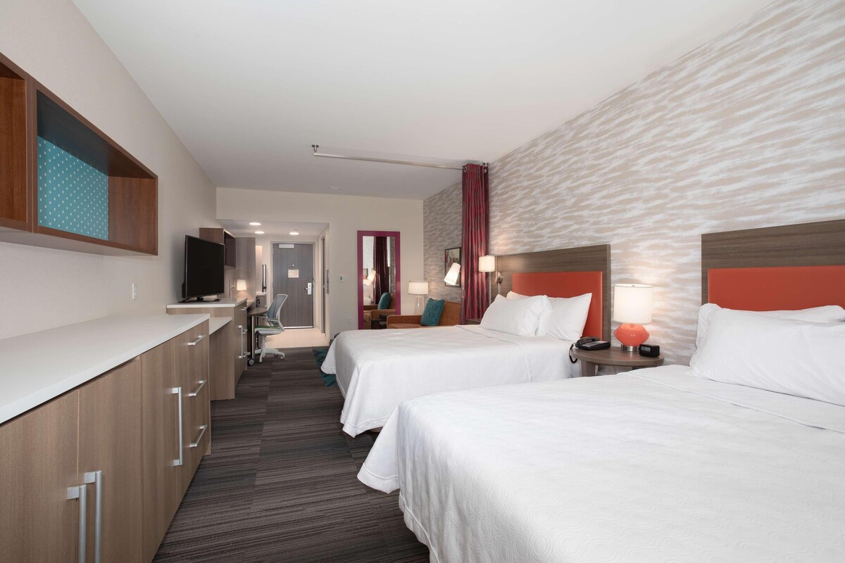 A hotel room with two beds, a desk, a TV, and a bathroom visible through an open door.