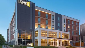 A modern hotel building with a prominent sign reading "HOME 2 Suites by Hilton."