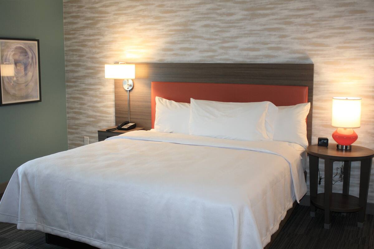 Een hotelkamer met een groot bed, twee bedlampen, een nachtkastje en een wandklok.