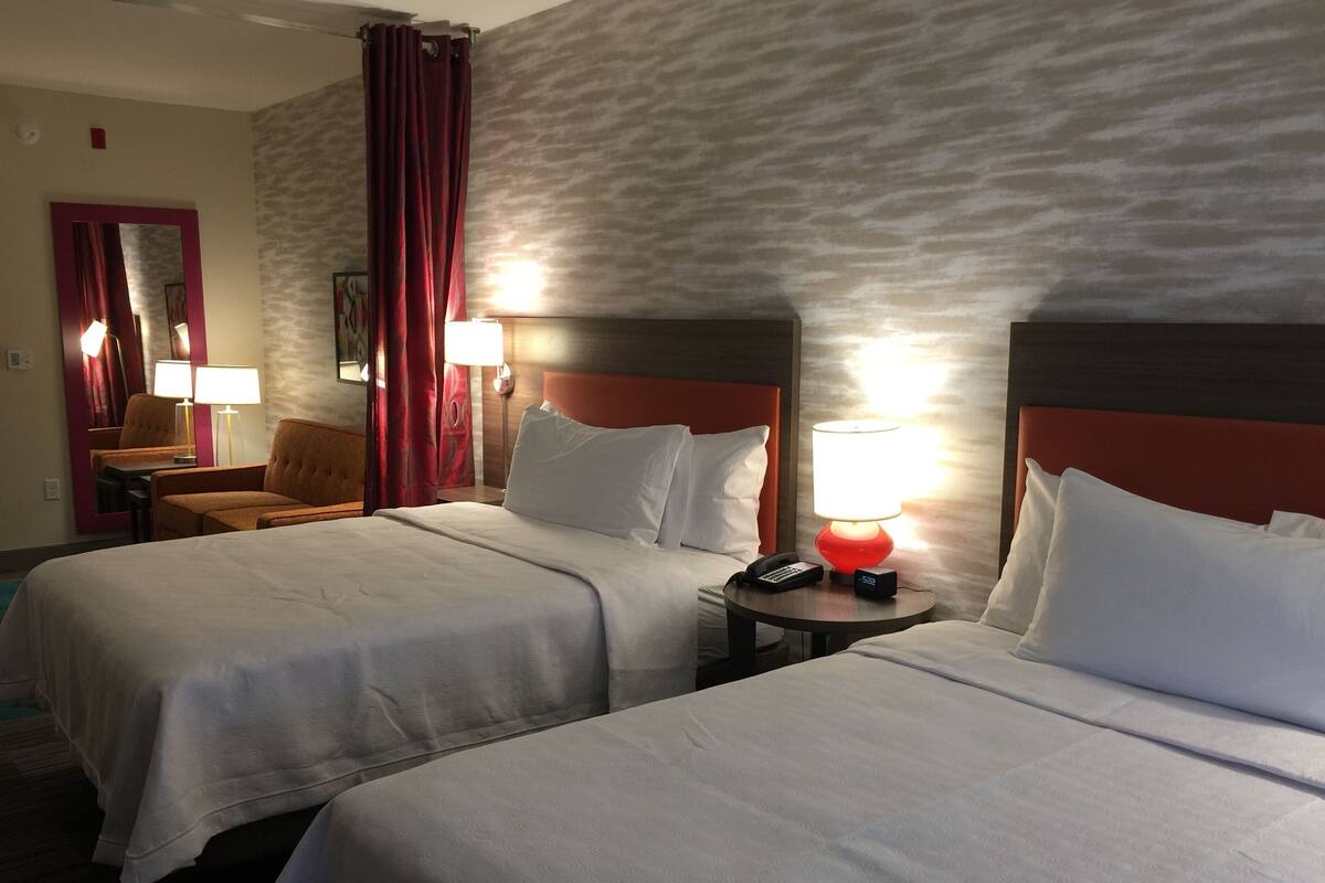 Een hotelkamer met twee bedden, een nachtkastje met een lamp, een stoel, een bureau en een spiegel.