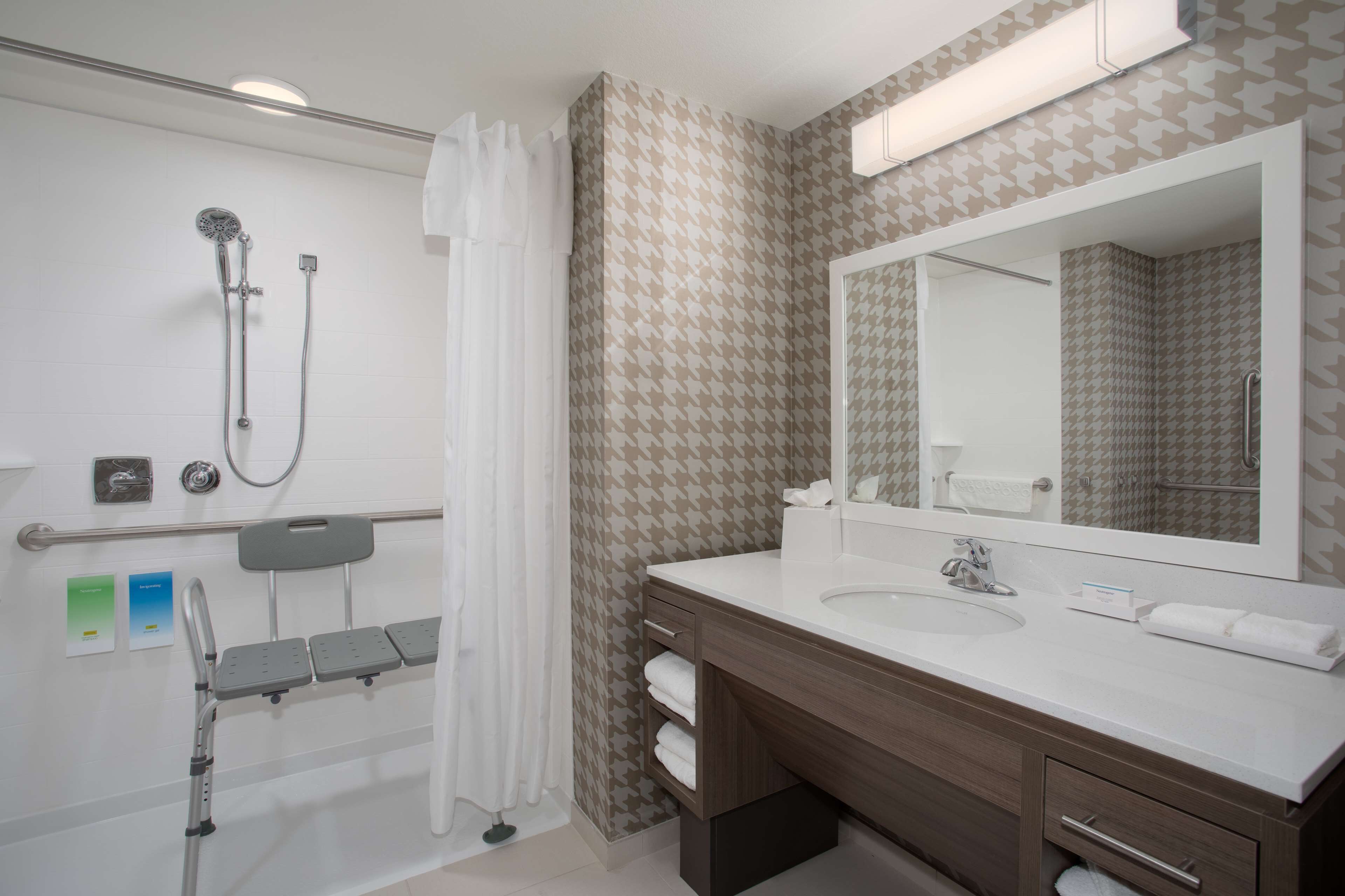 A modern bathroom with a shower, a vanity with a mirror, and a wheelchair-accessible bench.