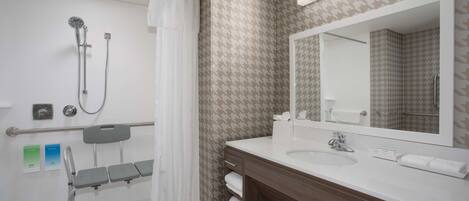 A modern bathroom with a shower, a vanity with a mirror, and a wheelchair-accessible bench.