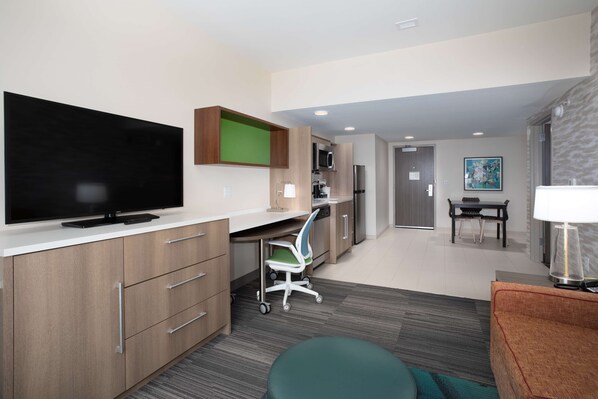Una habitación de hotel moderna con televisión de pantalla plana, un escritorio con silla, zona de comedor y sofá.