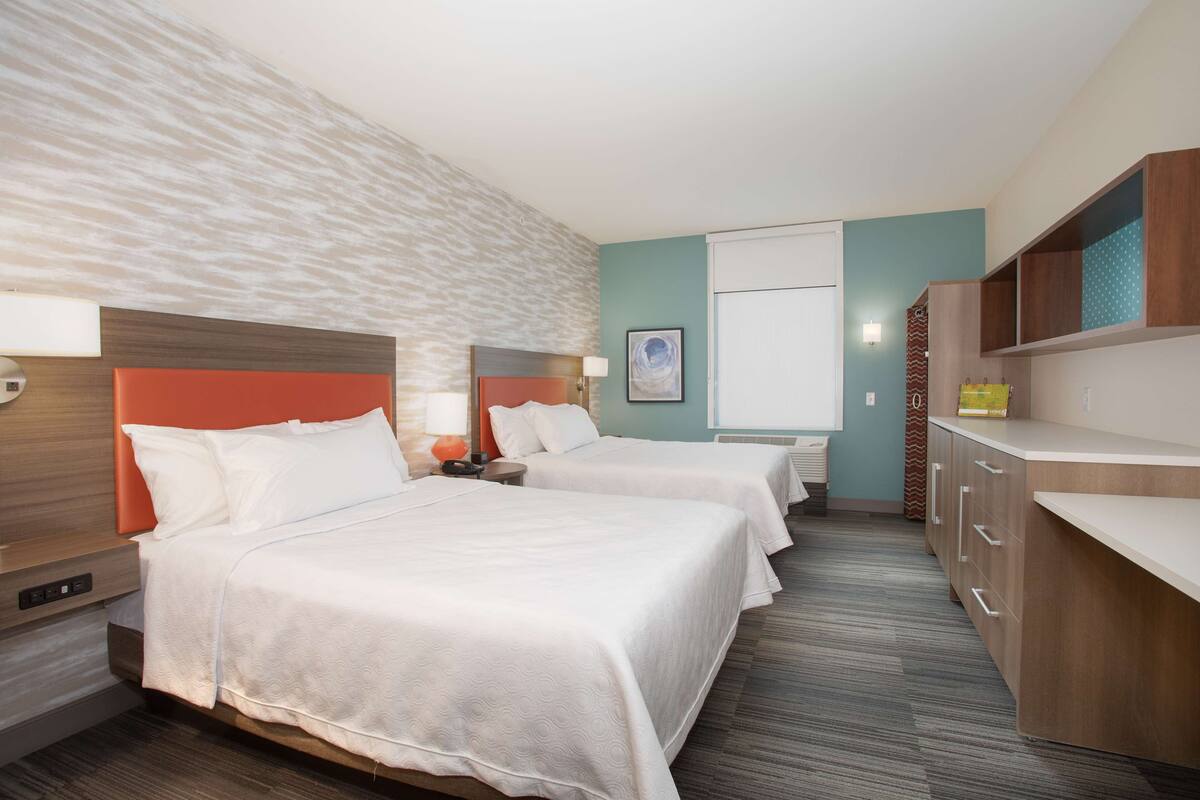 Een hotelkamer met twee bedden, een houten hoofdbord, een bureau en een kledingkast.