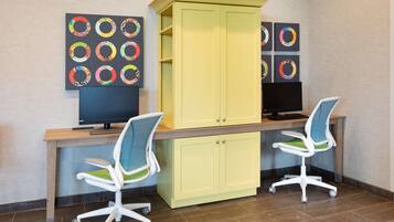 Un espace de travail comprenant deux chaises de bureau, un bureau, un écran d’ordinateur et un meuble jaune.