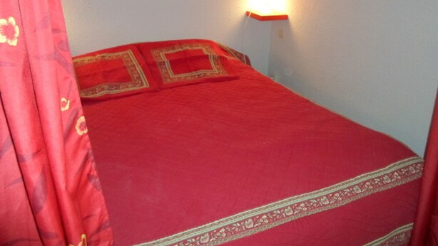 A bed with a red bedspread and a wall-mounted lamp.