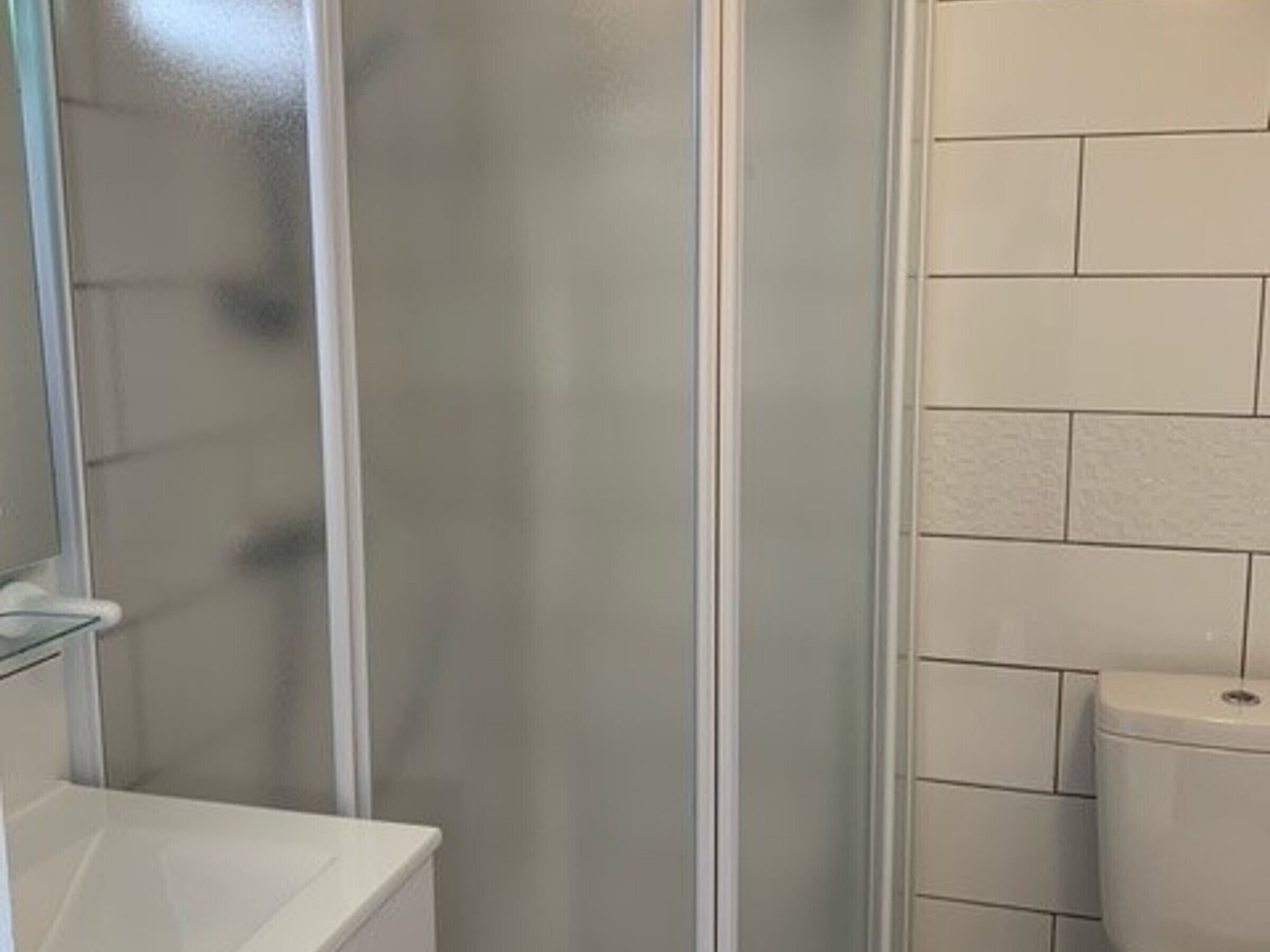 Ett badrum med en vit toalett, en duschkabin med glasväggar och en vit handfat.