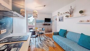 Een moderne woonkamer met een blauwe bank, een eettafel met stoelen, een televisie en een keuken met een grill.