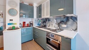 Een moderne keuken met grijze kastjes, een roestvrijstalen oven en een spatwand met een marmerachtig patroon.
