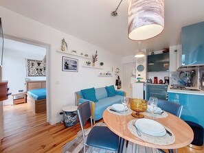 Un espacio habitable moderno con comedor, un sofá, una cocina y una pequeña mesa de comedor para dos.