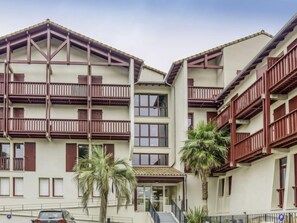 Un hotel de varios pisos con balcones, una entrada principal y palmeras.