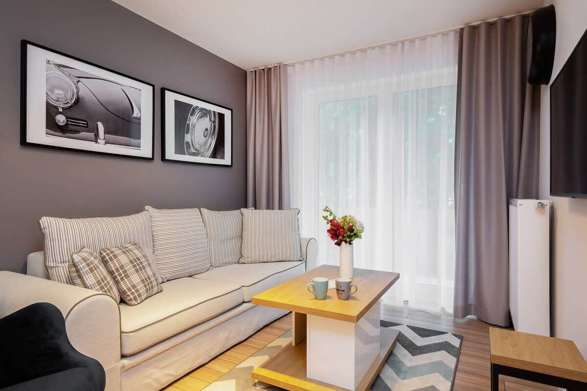 A modern, comfortable living room with a beige sofa, coffee table, and stylish decor pieces. Large windows bring in plenty of light, making it a bright and inviting space.