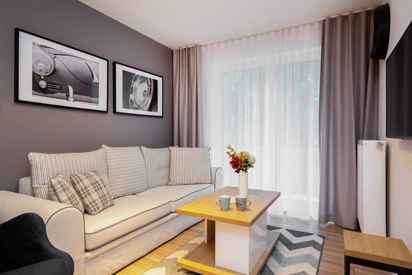 A modern, comfortable living room with a beige sofa, coffee table, and stylish decor pieces. Large windows bring in plenty of light, making it a bright and inviting space.