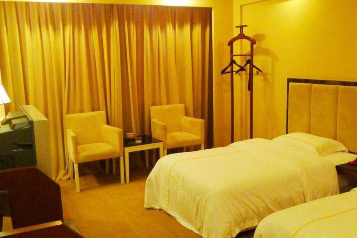 Habitación de hotel con dos camas, un escritorio, una silla y un perchero.