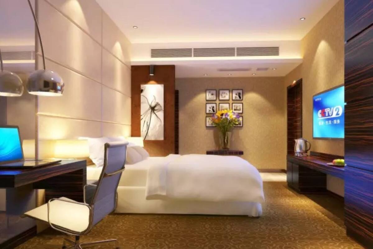 Una habitación de hotel moderna con cama, escritorio, silla, televisor y una obra de arte en la pared.