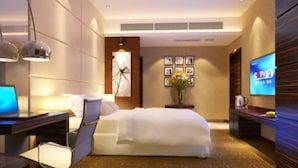 A modern hotel room with a bed, desk, chair, TV, and artwork on the wall. - Junyue Hotel (Zhaoqing)