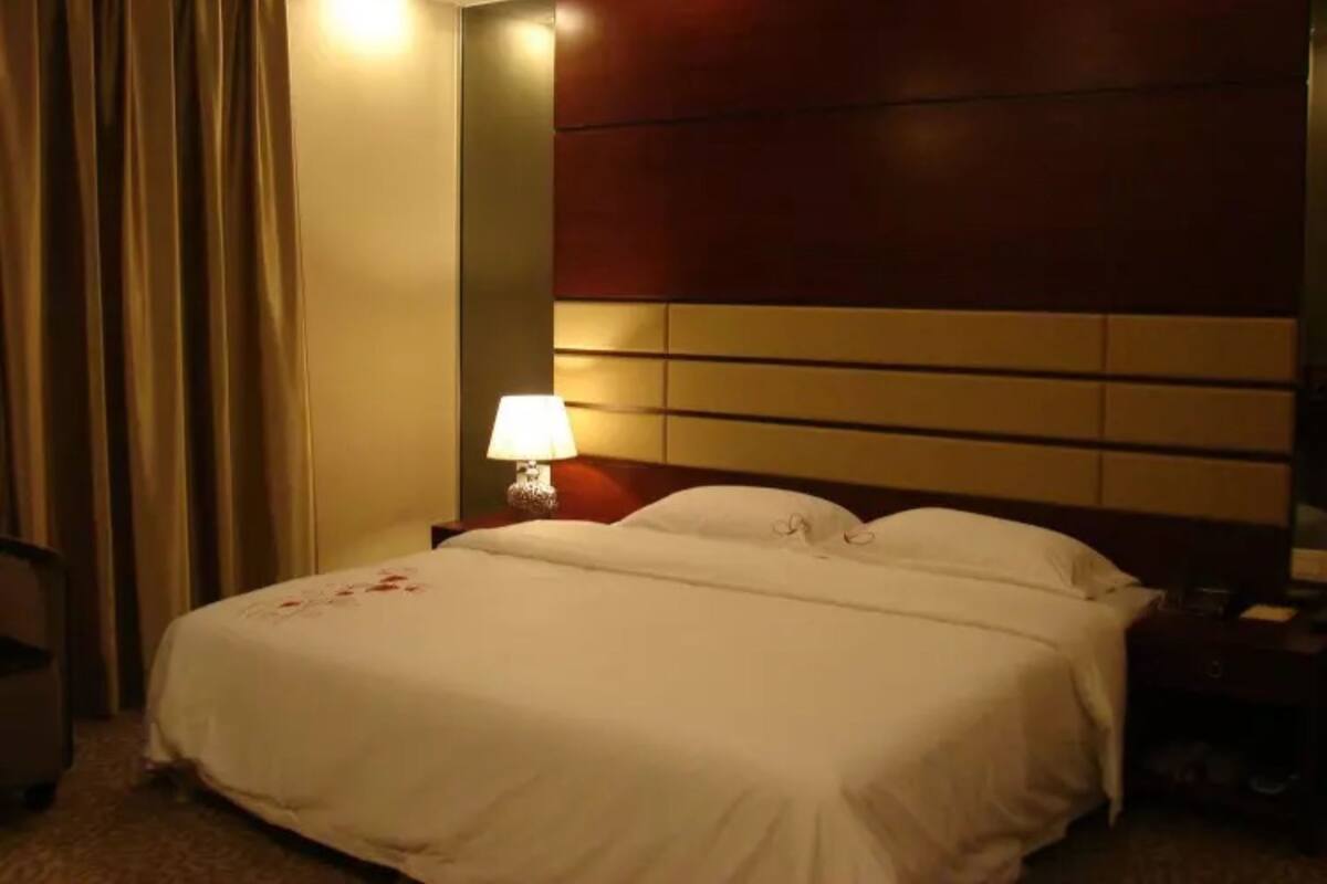Una habitación de hotel con una cama grande, una mesita de noche con lámpara y un cabecero de madera.