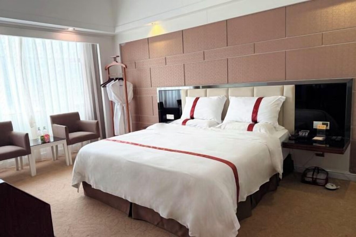 A hotel room with a large bed, a desk, a chair, and a wardrobe.