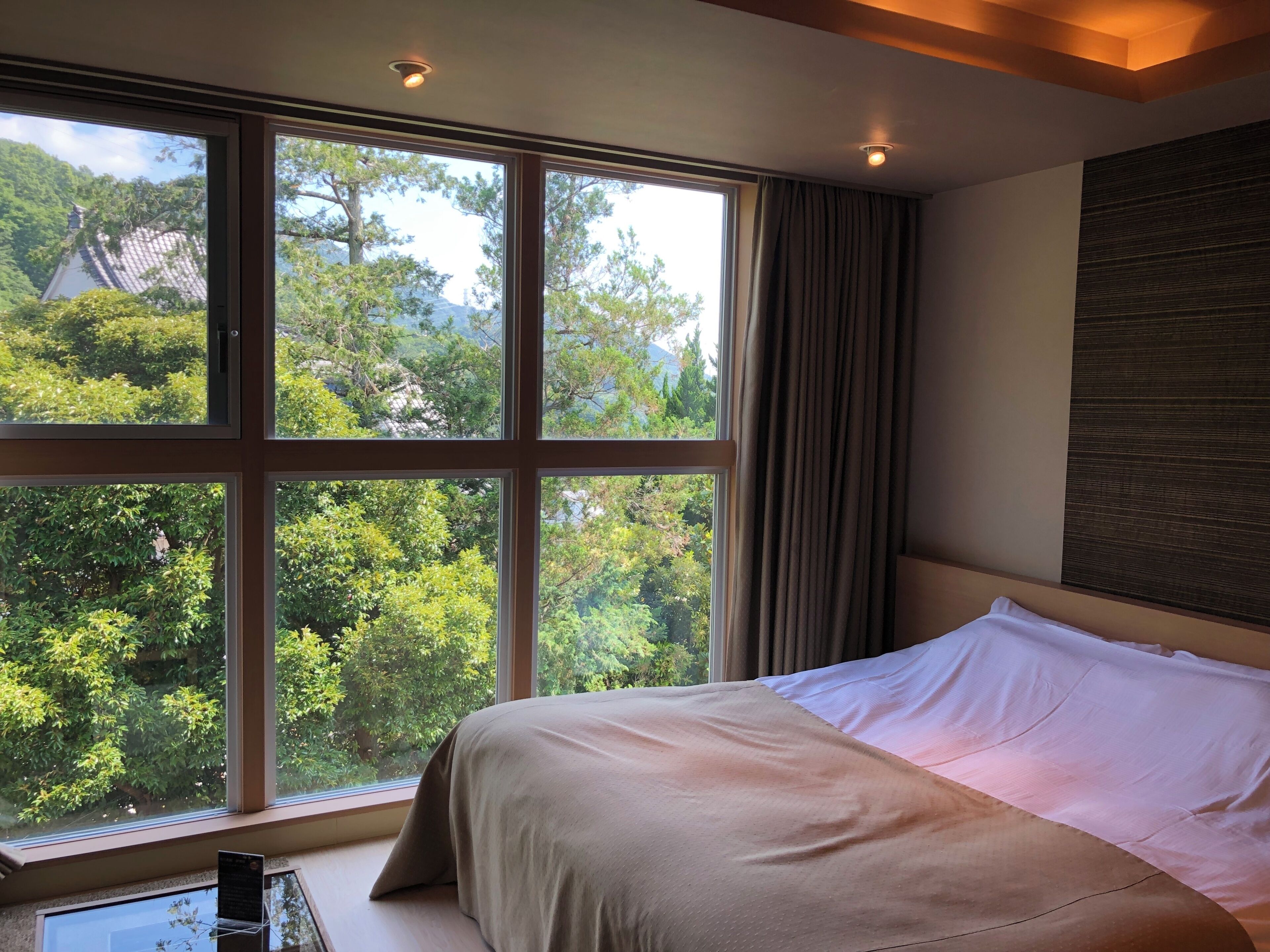 A bedroom with a large window, a bed, and a view of greenery.