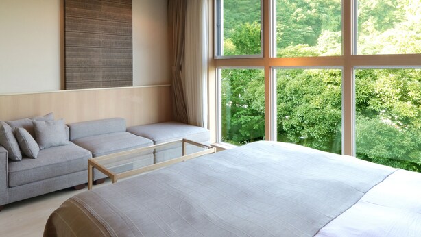 Un dormitorio moderno con una cama grande, un sofá y una ventana que ofrece vistas a zonas verdes.