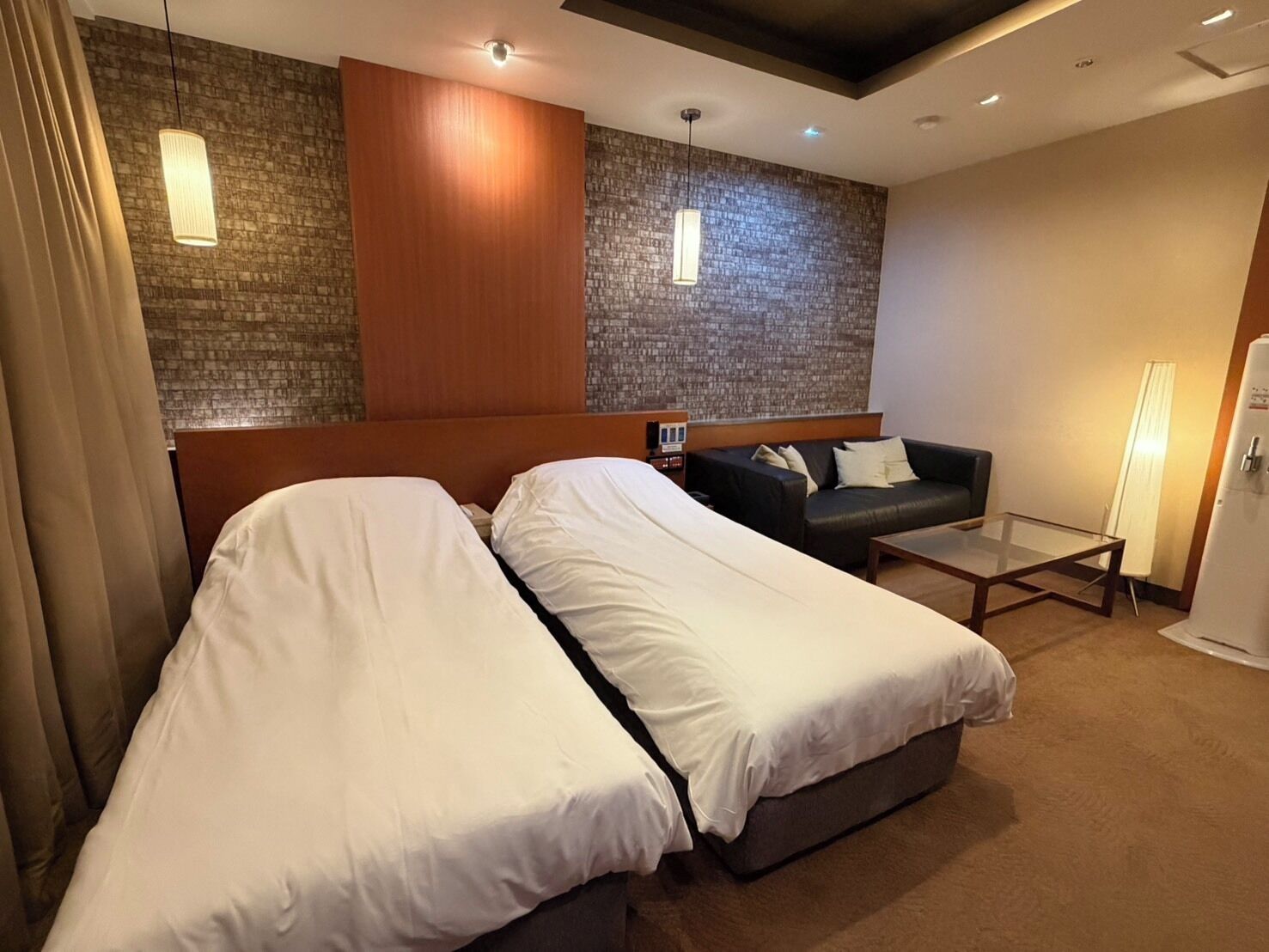A hotel room with two beds, a sofa, a small table, and a refrigerator.