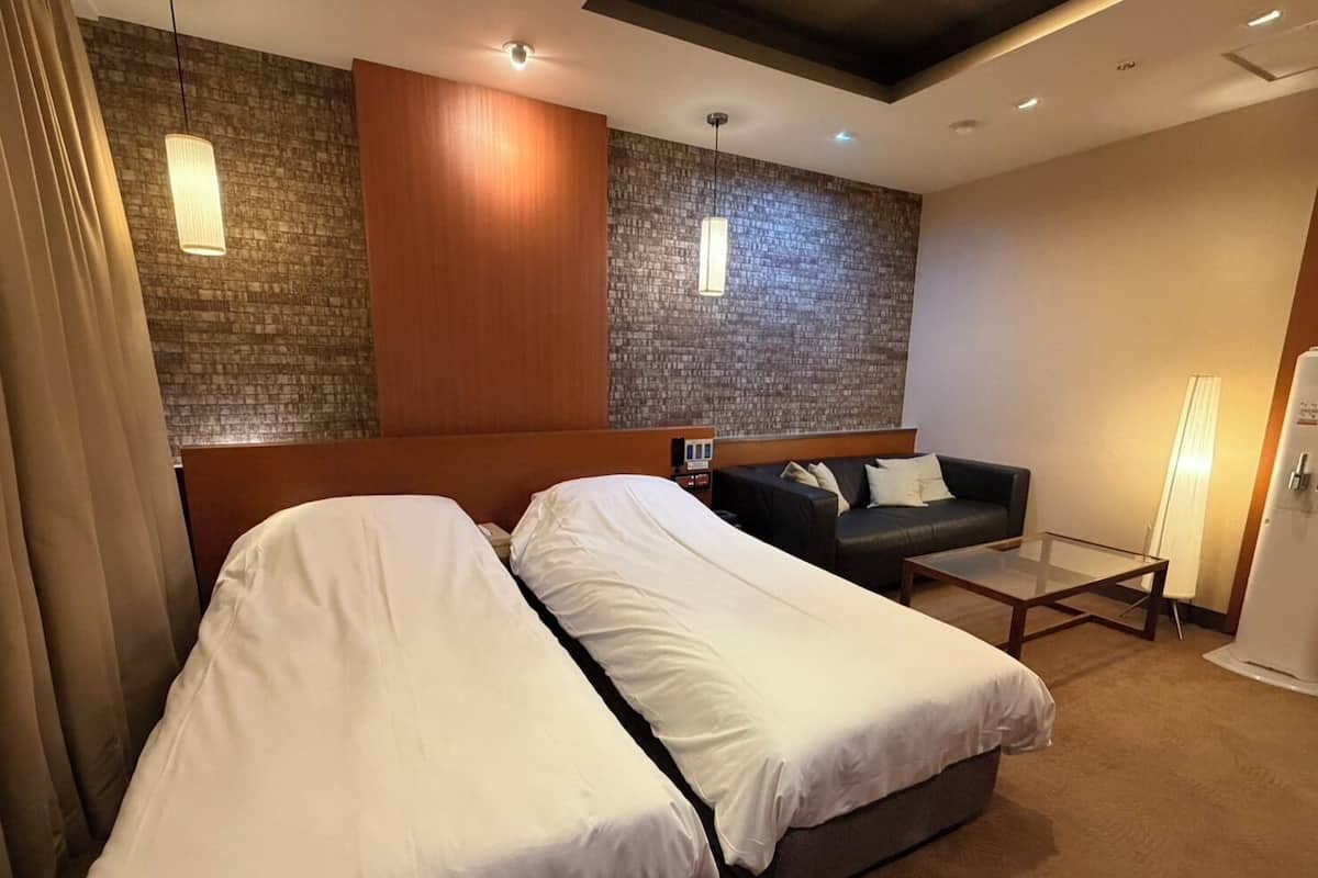 A hotel room with two beds, a sofa, a small table, and a refrigerator.