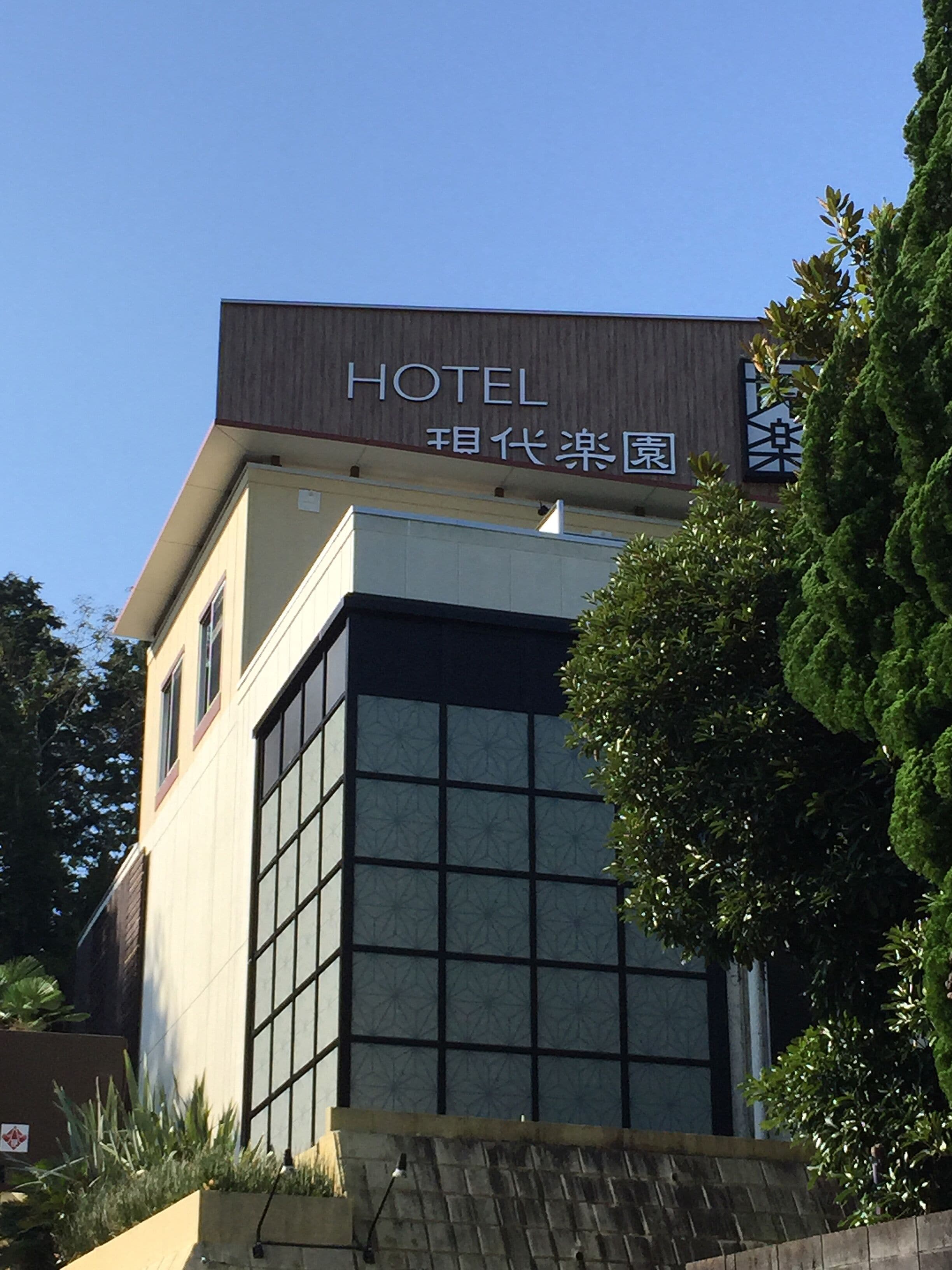 A hotel building with a modern design, featuring large windows and a sign that reads "HOTEL" in English and another language.
