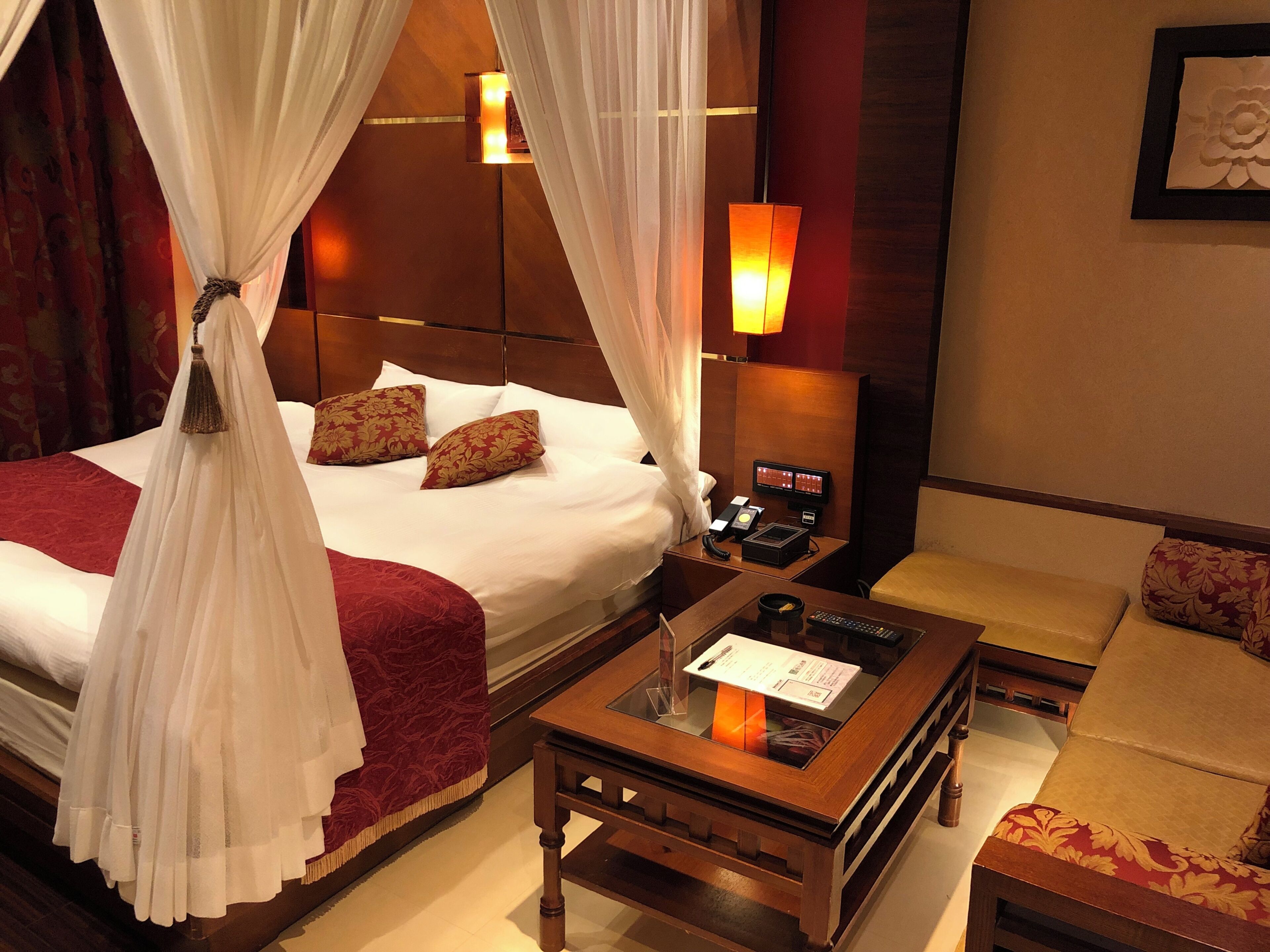 A hotel room with a bed, a bedside table with a lamp, a chair, and a small table with a menu.