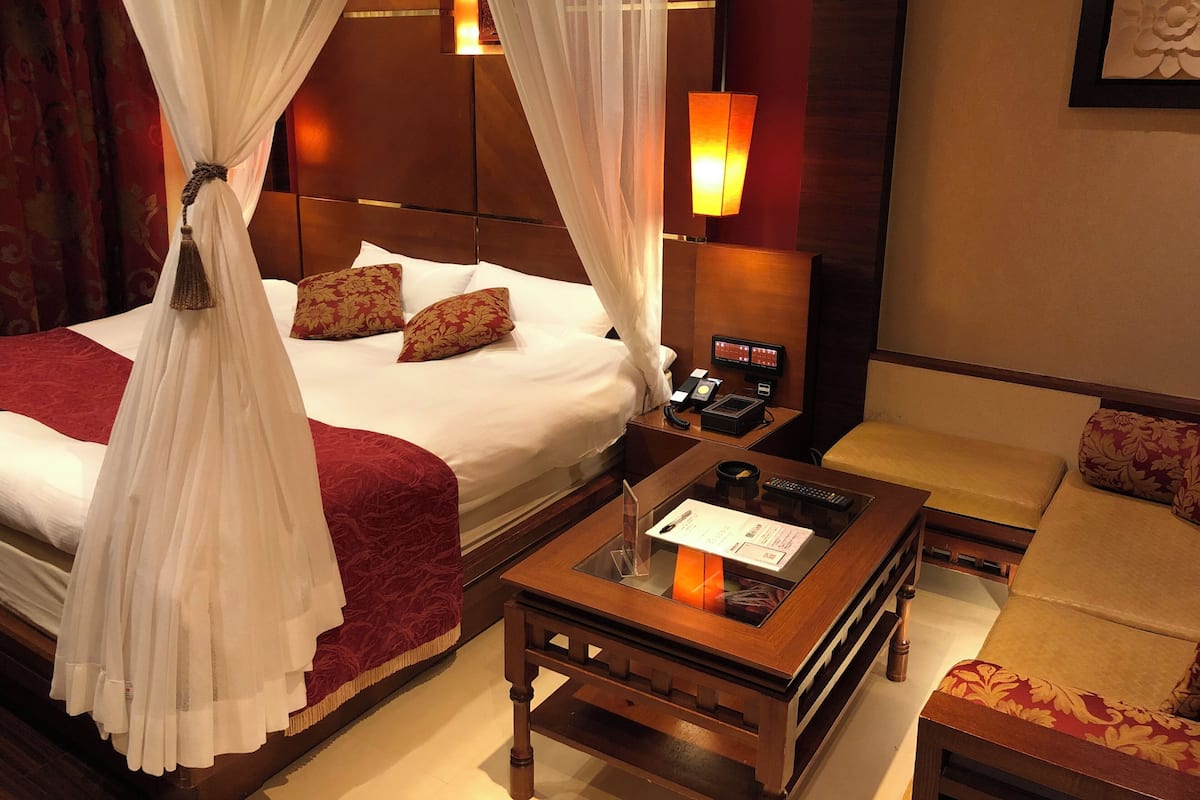 A hotel room with a bed, a bedside table with a lamp, a chair, and a small table with a menu.