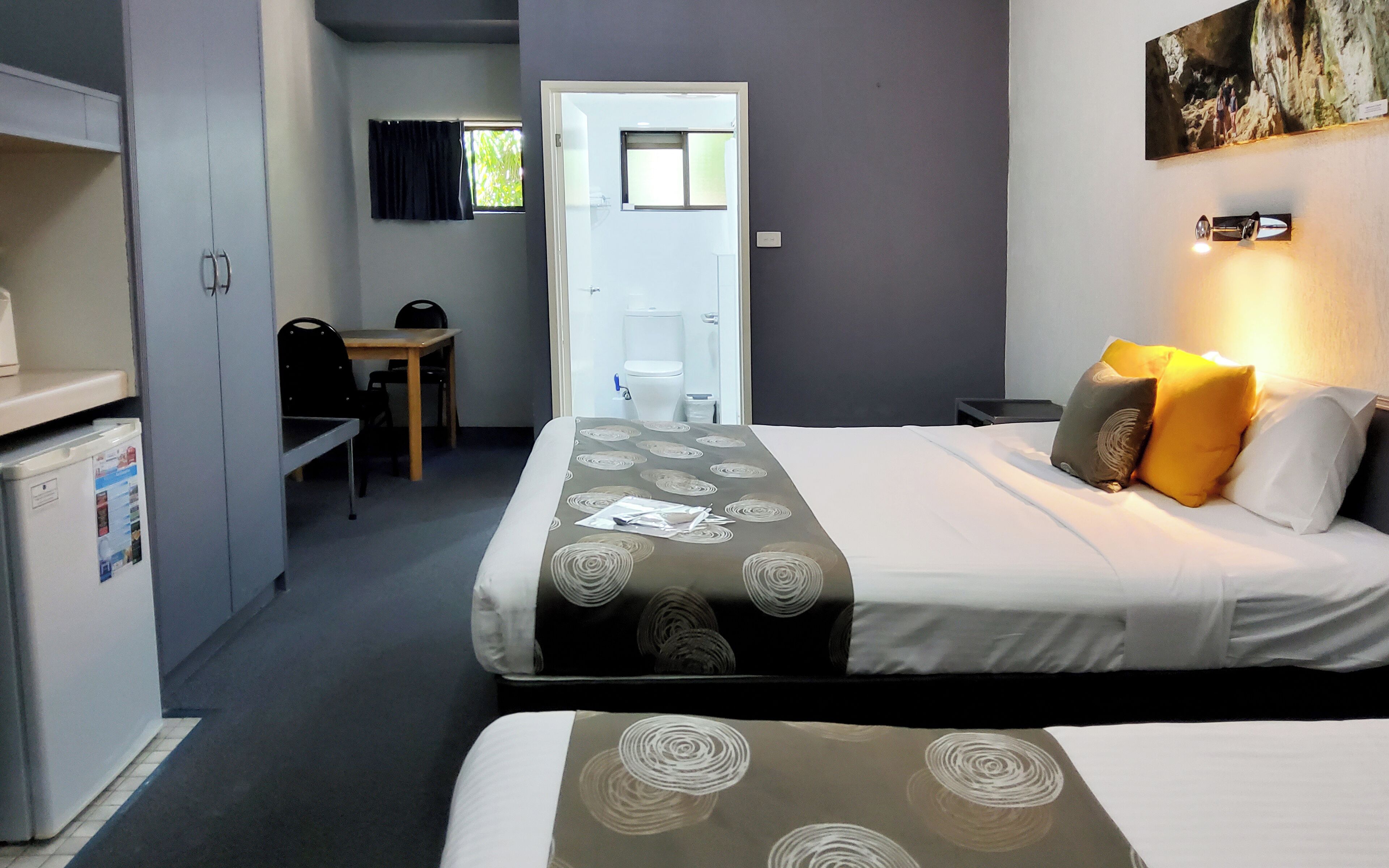 Habitación de hotel con cama, escritorio y silla. Hay una puerta que da al baño y a un pasillo.