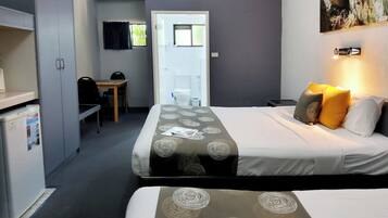 Habitación de hotel con cama, escritorio y silla. Hay una puerta que da al baño y a un pasillo.